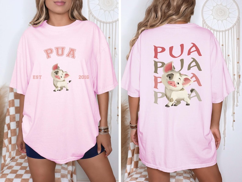 May include: Pale pink oversized t-shirt with a cartoon pig design. The front displays "PUA" above the pig, with "EST 2016" below. The back of the shirt has "PUA" repeated three times in a vertical pattern.