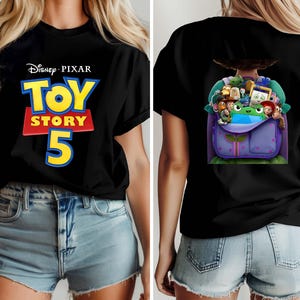 K&ouml;nnte beinhalten: Ein schwarzes T-Shirt mit dem Disney Pixar Toy Story 5 Logo in Gelb, Rot und Blau auf der Vorderseite. Die R&uuml;ckseite des T-Shirts zeigt eine Grafik eines violetten Rucksacks, der mit verschiedenen animierten Figuren gef&uuml;llt ist, darunter eine gr&uuml;ne Figur.