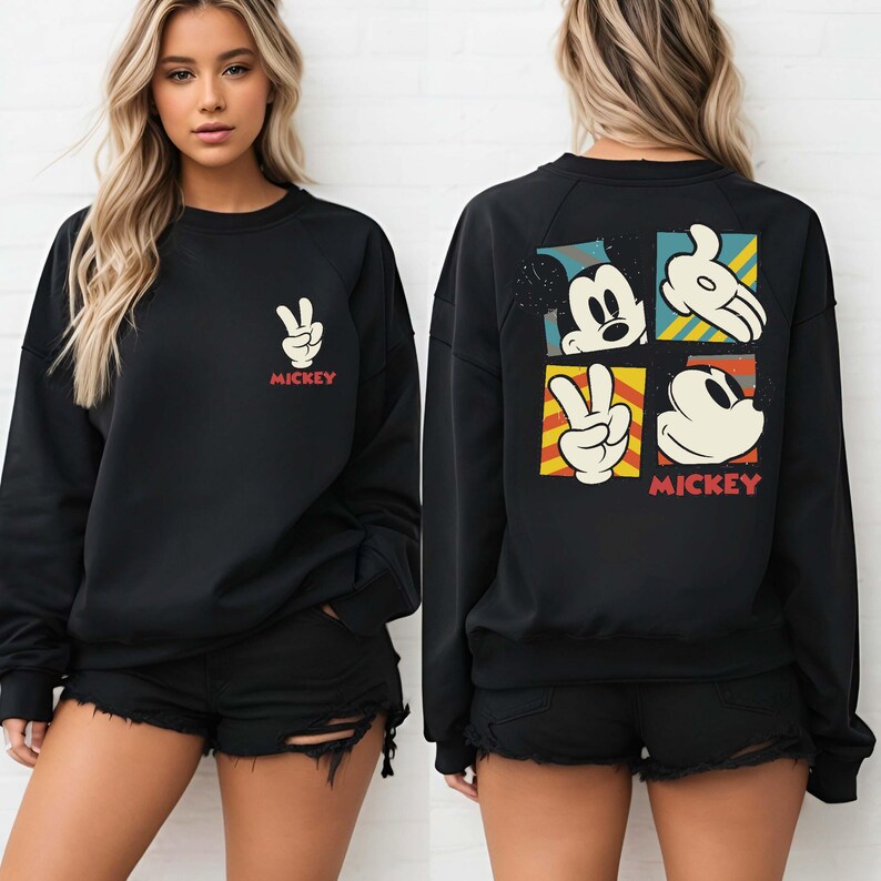 May include: Black sweatshirt featuring a Mickey Mouse design. The front displays a peace sign with the word "Mickey" in red. The back showcases Mickey Mouse's face, hand, and peace sign in a colorful, square pattern. A casual, comfortable top.