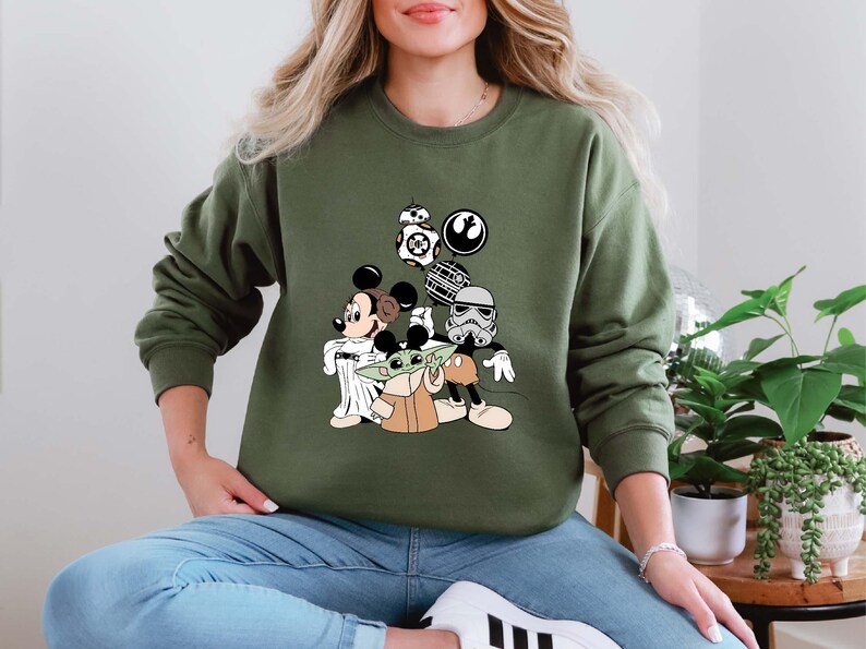 Puede incluir: Sudadera verde oliva con un dise&ntilde;o de Mickey Mouse como Jedi, Baby Yoda y otros personajes de Star Wars. El dise&ntilde;o incluye a BB-8, un Stormtrooper y el s&iacute;mbolo de la Alianza Rebelde. La sudadera es de cuello redondo.