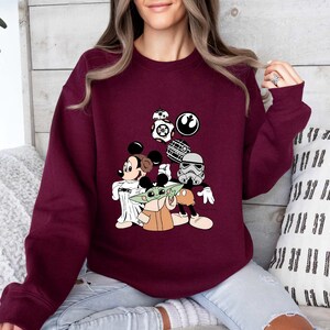 Puede incluir: Una sudadera granate con un dise&ntilde;o de Mickey Mouse, Baby Yoda y personajes de Star Wars. El dise&ntilde;o incluye a BB-8, un Stormtrooper y la Estrella de la Muerte. La sudadera es de manga larga.