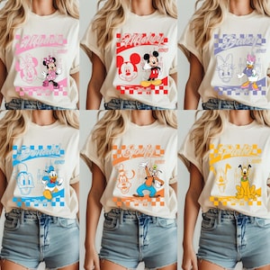 May include: Six cream-colored t-shirts featuring Disney characters. Each shirt has a different character design: Minnie Mouse, Mickey Mouse, Daisy Duck, Donald Duck, Goofy, and Pluto. The designs include character illustrations and names.