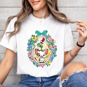 Puede incluir: Camiseta blanca con un gr&aacute;fico colorido de un cerdo y un gallo, rodeados de flores y un lazo turquesa. El dise&ntilde;o est&aacute; enmarcado en un c&iacute;rculo con un fondo amarillo. Una prenda casual para el d&iacute;a a d&iacute;a.