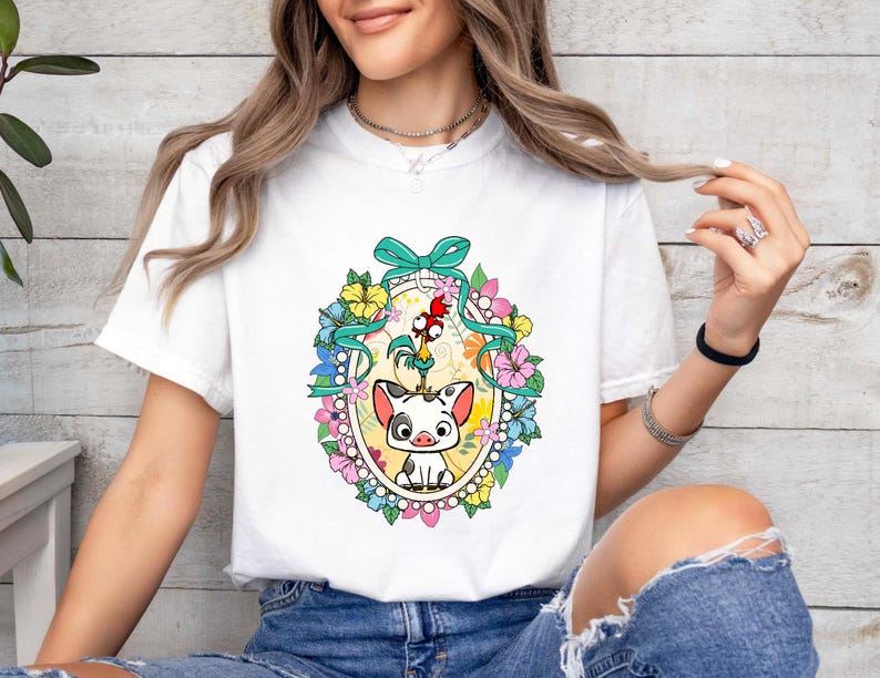 Puede incluir: Camiseta blanca con un gr&aacute;fico colorido de un cerdo y un gallo, rodeados de flores y un lazo turquesa. El dise&ntilde;o est&aacute; enmarcado en un c&iacute;rculo con un fondo amarillo. Una prenda casual para el d&iacute;a a d&iacute;a.