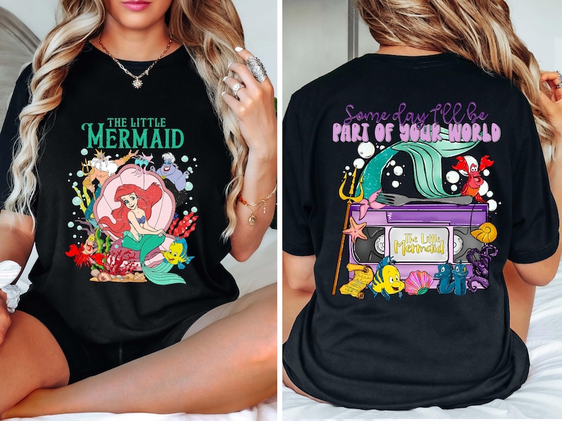 May include: Black t-shirt featuring a colorful graphic from "The Little Mermaid." The front design includes Ariel, Flounder, and Sebastian. The back design shows a VHS tape with the text "Some day I'll be part of your world."