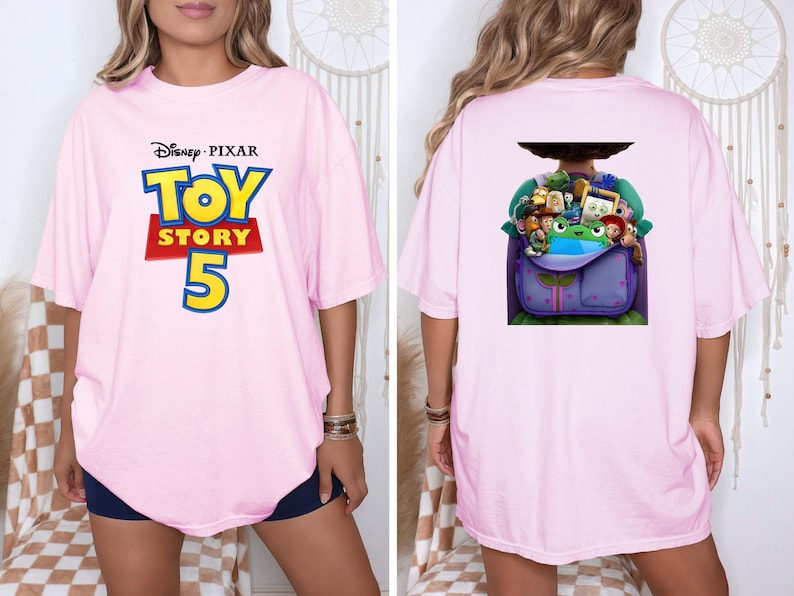 K&ouml;nnte beinhalten: Ein hellrosa T-Shirt mit dem Disney Pixar Toy Story 5 Logo auf der Vorderseite. Die R&uuml;ckseite des Shirts zeigt eine Grafik eines violetten Rucksacks, der mit verschiedenen animierten Spielfiguren gef&uuml;llt ist, darunter eine gr&uuml;ne Froschfigur.