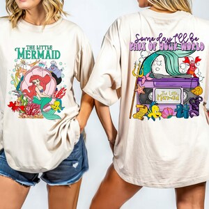 May include: Beige t-shirt featuring a colorful graphic from Disney's The Little Mermaid. The front design includes Ariel, Flounder, and Sebastian. The back of the shirt has a VHS tape design with the text "Some day I'll be part of your world."