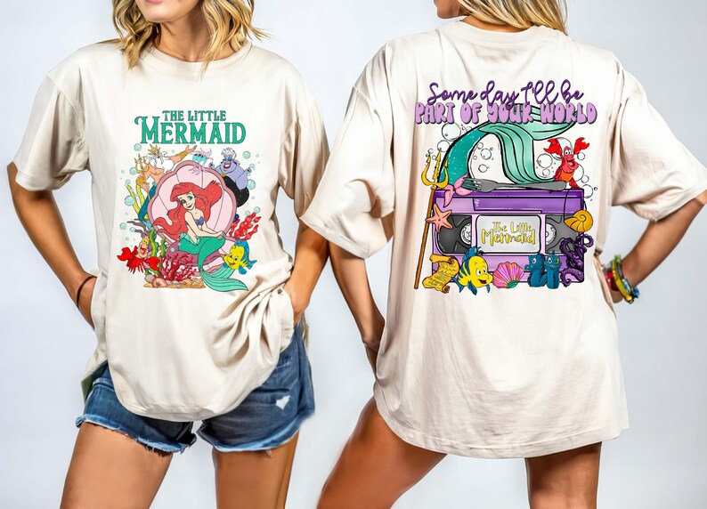 May include: Beige t-shirt featuring a colorful graphic from Disney's The Little Mermaid. The front design includes Ariel, Flounder, and Sebastian. The back of the shirt has a VHS tape design with the text "Some day I'll be part of your world."