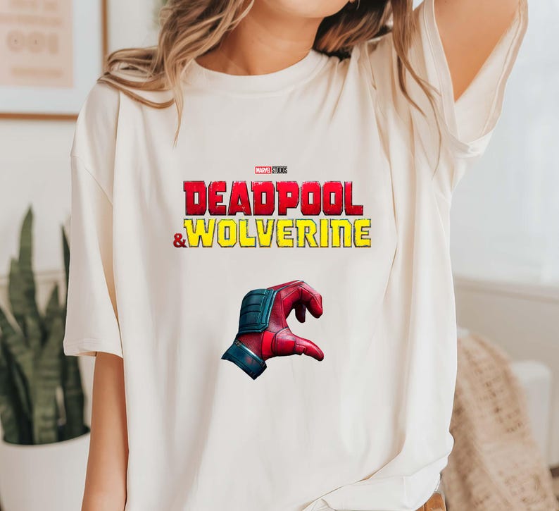 Puede incluir: Camiseta color crema con el texto "DEADPOOL & WOLVERINE" en rojo y amarillo, con un logo de Marvel Studios. Debajo, un gr&aacute;fico de una mano roja y azul.