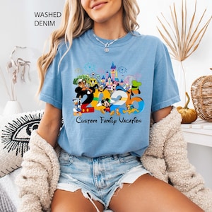May include: Light blue t-shirt with a colorful graphic featuring Disney characters and the text "2020 Custom Family Vacation." The shirt is made of washed denim material.