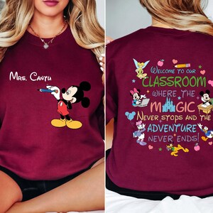 K&ouml;nnte beinhalten: Burgunderfarbenes Sweatshirt mit Mickey Mouse, der einen Bleistift h&auml;lt, und dem Namen "Mrs. Cantu". Auf der R&uuml;ckseite des Shirts befindet sich ein farbenfrohes Design mit Disney-Figuren und dem Text "Welcome to our classroom where the magic never stops and the adventure never ends!"