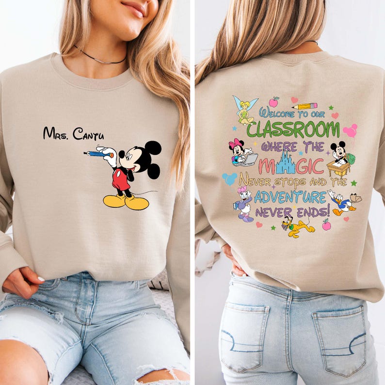 K&ouml;nnte beinhalten: Beiges Sweatshirt mit Mickey Mouse, der einen Stift h&auml;lt, und dem Text "Mrs. Cantu" auf der Vorderseite. Auf der R&uuml;ckseite steht "Welcome to our Classroom where the Magic Never Stops and the Adventure Never Ends!" mit Disney-Figuren.