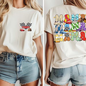 May include: Cream-colored t-shirt featuring a front pocket design with checkered flags, a red race car, and a brown truck. The back of the shirt displays the word "MAMA" in colorful, car-themed letters, with the number "95".