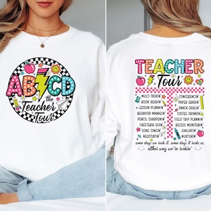 May include: White sweatshirt with a colorful graphic on the front that says "AB7CD the Teacher Tour". The back of the sweatshirt has a list of teacher-related activities. The design includes an apple, pencil, and lightning bolt.