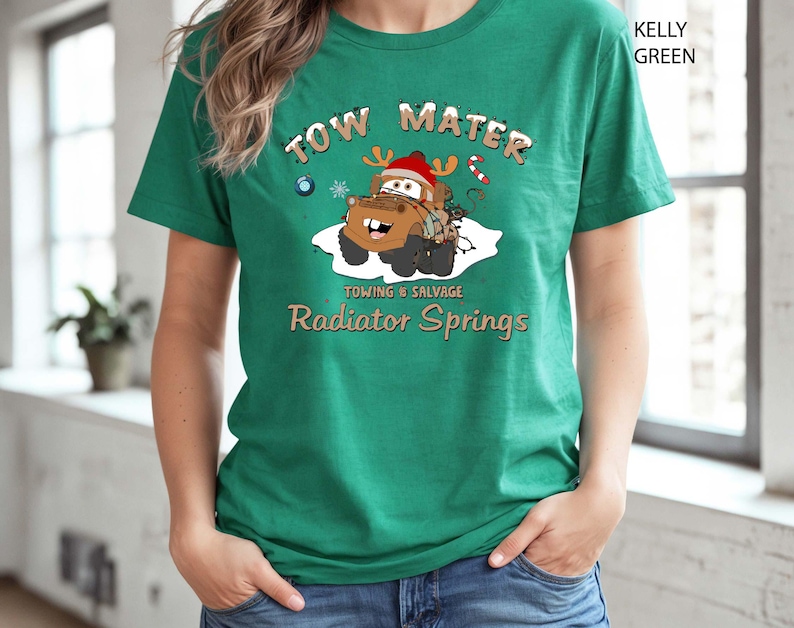 May include: Kelly green t-shirt featuring a cartoon image of Tow Mater from the movie Cars, wearing a Santa hat and reindeer antlers. The text "TOW MATER" and "Towing & Salvage, Radiator Springs" are printed above and below the image.
