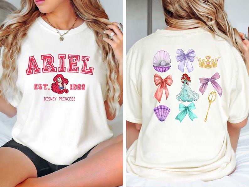 Może przedstawiać: Kremowa koszulka z napisem "ARIEL" w czerwonym stylu uniwersyteckim, z wizerunkiem Ariel i napisem "EST. 1989 DISNEY PRINCESS." Tył przedstawia ilustracje z motywem Ariel: kokardy, muszle, koronę i tr&oacute;jząb.