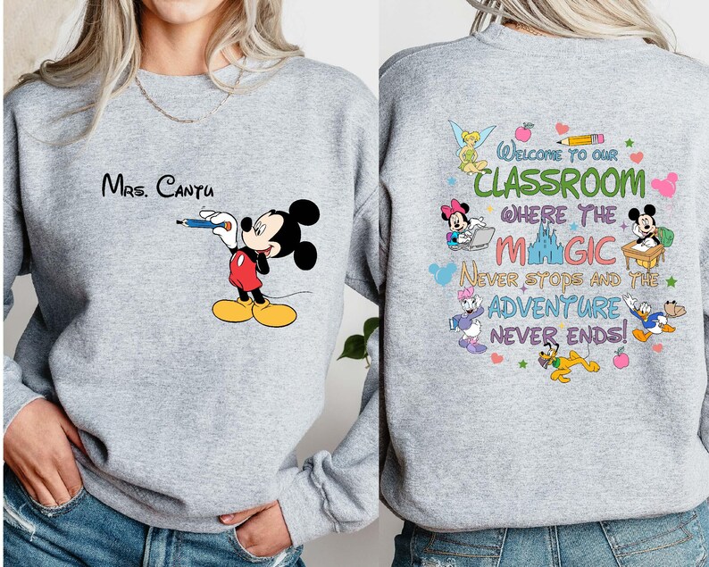 K&ouml;nnte beinhalten: Hellgraues Sweatshirt mit Mickey Mouse, der mit einem blauen Stift zeichnet. Der Text "Mrs. Cantu" steht &uuml;ber Mickey. Auf der R&uuml;ckseite des Sweatshirts steht "Welcome to our classroom where the magic never stops and the adventure never ends!"