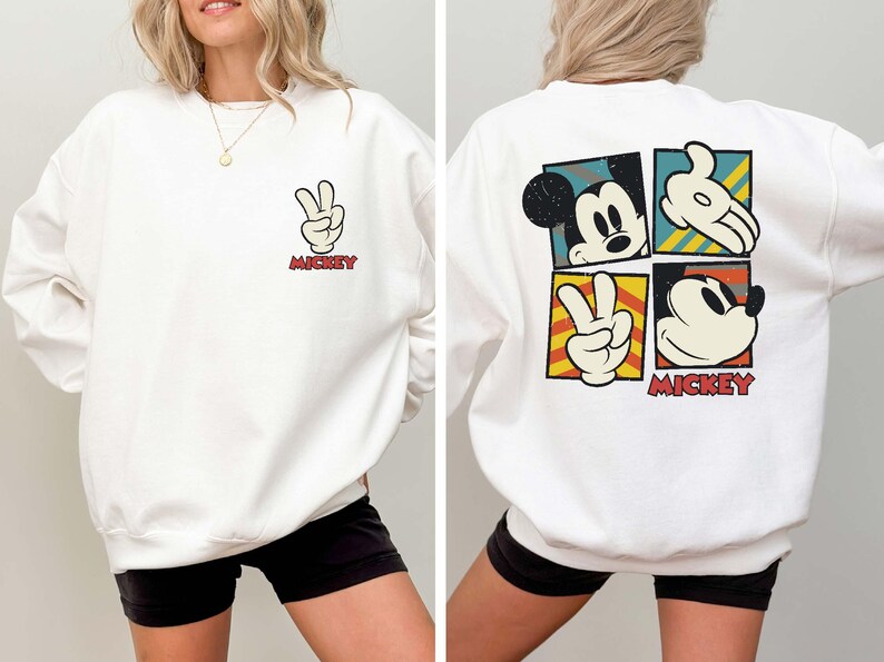 May include: White sweatshirt featuring a Mickey Mouse design. The front displays a peace sign hand gesture with the word "Mickey" in red. The back has four squares with Mickey Mouse images and the word "Mickey".
