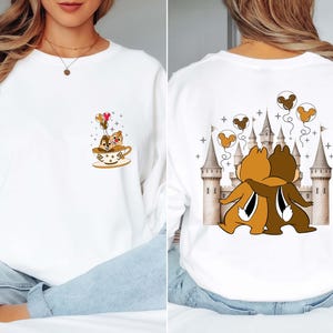 May include: White sweatshirt featuring a Chip and Dale design. The front shows the chipmunks in a teacup with balloons. The back displays the chipmunks hugging in front of a castle with Mickey Mouse balloons. A cute and whimsical design.
