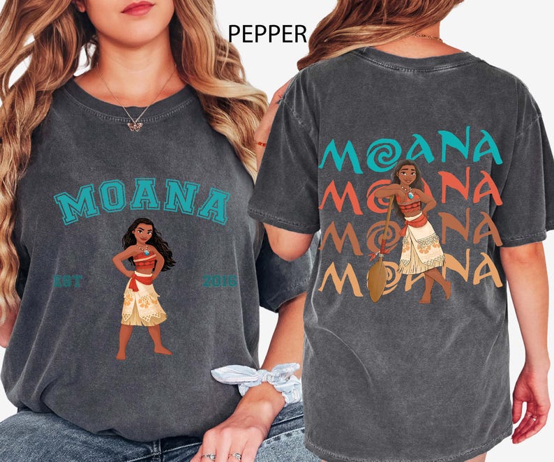 May include: Charcoal grey t-shirt with the word "MOANA" in teal, and an illustration of Moana. The back of the shirt repeats "MOANA" in teal, orange, and yellow, with a Moana illustration. The shirt is a crew neck.