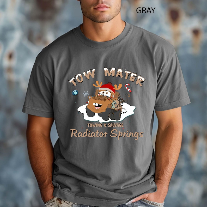 May include: Gray t-shirt featuring a cartoon image of Tow Mater from the movie Cars, wearing a Santa hat and reindeer antlers. The text "TOW MATER" is above the image, and "Towing & Salvage, Radiator Springs" is below.