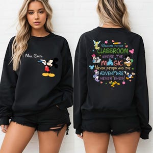 K&ouml;nnte beinhalten: Schwarzes Sweatshirt mit Mickey Mouse, der einen Stift h&auml;lt, und dem Text "Mrs. Cantu" dar&uuml;ber. Auf der R&uuml;ckseite des Sweatshirts steht "Welcome to our Classroom where the Magic Never Stops and the Adventure Never Ends!" mit Disney-Figuren.