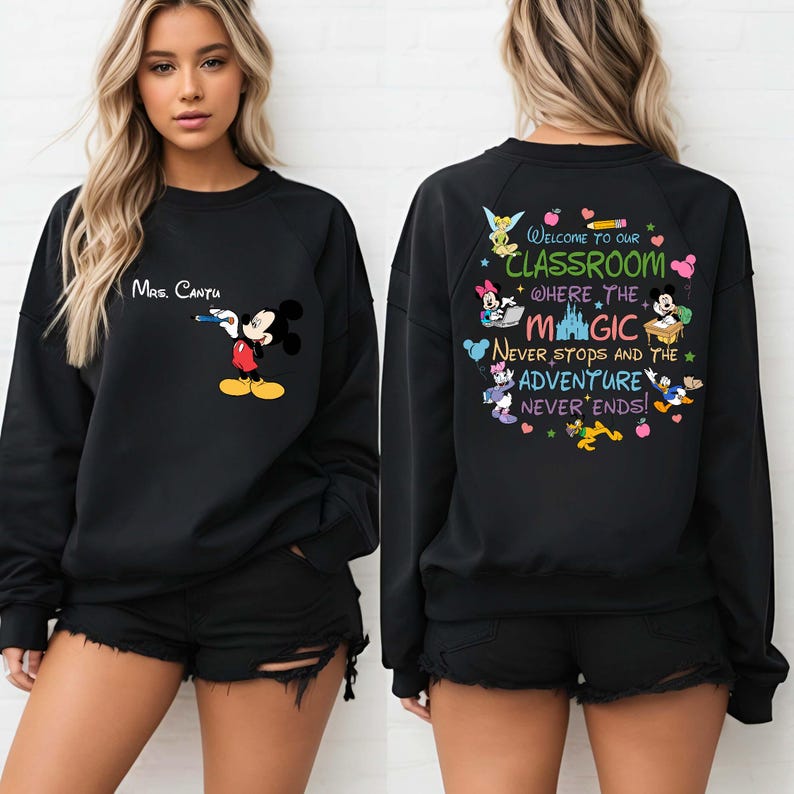 K&ouml;nnte beinhalten: Schwarzes Sweatshirt mit Mickey Mouse, der einen Stift h&auml;lt, und dem Text "Mrs. Cantu" dar&uuml;ber. Auf der R&uuml;ckseite des Sweatshirts steht "Welcome to our Classroom where the Magic Never Stops and the Adventure Never Ends!" mit Disney-Figuren.