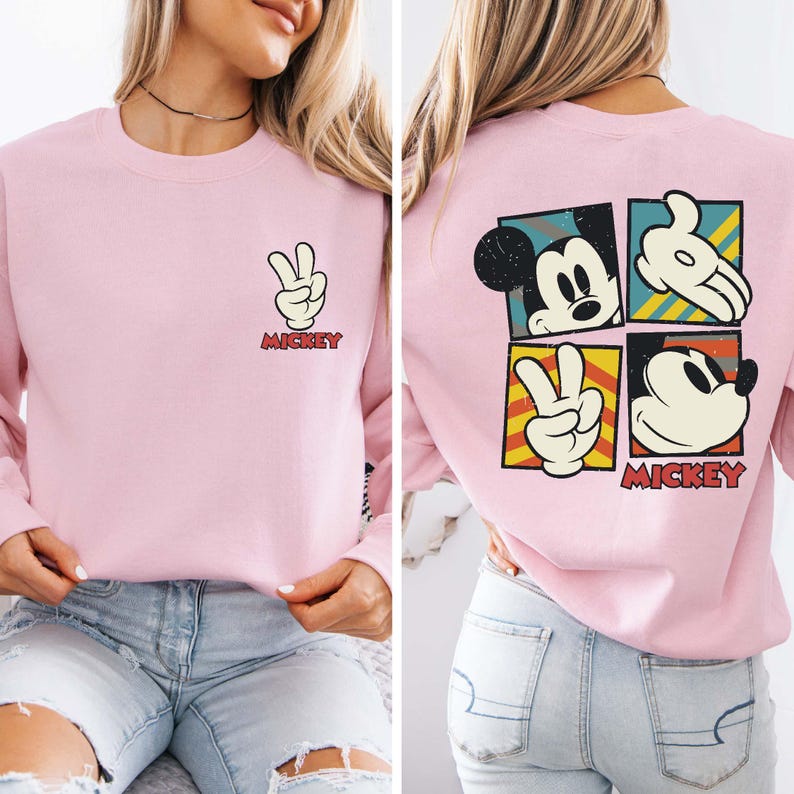 May include: Light pink sweatshirt featuring Mickey Mouse imagery. The front displays a peace sign with the word "Mickey." The back showcases four Mickey Mouse-themed squares. The sweatshirt is a casual, comfortable style.