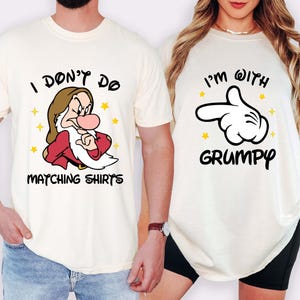 May include: Two cream-coloured t-shirts. One features an illustration of Grumpy from Snow White with the text "I DON'T DO MATCHING SHIRTS." The other shirt has a pointing hand graphic and the text "I'M WITH GRUMPY."