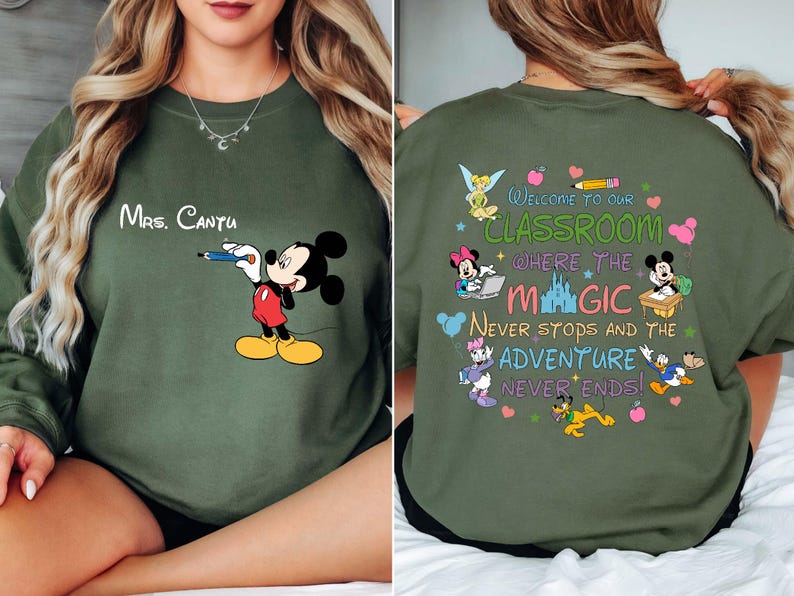 K&ouml;nnte beinhalten: Ein olivgr&uuml;nes Sweatshirt mit Mickey Mouse, der einen Bleistift h&auml;lt, und dem Namen "Mrs. Cantu" dar&uuml;ber. Auf der R&uuml;ckseite befindet sich ein farbenfrohes Design mit Disney-Figuren und dem Text "Welcome to our classroom where the magic never stops and the adventure never ends!"