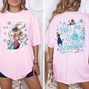 May include: Light pink t-shirt featuring characters from the animated film Frozen. The front displays Elsa, Anna, Olaf, and Sven with snowflakes. The back has the text "Meet me in Arendelle" with other characters and snowflakes.