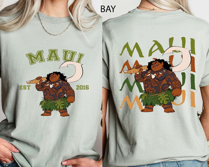 May include: A light green t-shirt with a cartoon illustration of Maui holding a fish hook. The front of the shirt has the word "MAUI" in green, with "EST 2016" below. The back of the shirt repeats "MAUI" in green, orange, and light green.