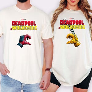 Puede incluir: Camisetas color crema con el texto "DEADPOOL & WOLVERINE" en rojo y amarillo. Una camiseta muestra una mano roja y azul, la otra una mano amarilla con garras. Son prendas informales.