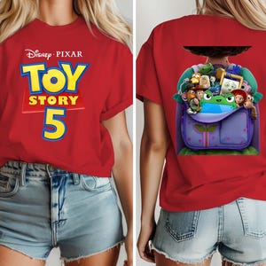 K&ouml;nnte beinhalten: Ein rotes T-Shirt mit kurzen &Auml;rmeln und dem Disney Pixar Toy Story 5 Logo in Gelb und Blau auf der Vorderseite. Die R&uuml;ckseite zeigt eine Grafik eines violetten Rucksacks, der mit verschiedenen animierten Figuren gef&uuml;llt ist, darunter ein gr&uuml;ner Frosch.
