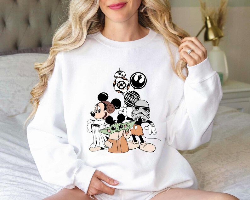 Puede incluir: Sudadera blanca con un dise&ntilde;o de Mickey Mouse, Baby Yoda y personajes de Star Wars. El dise&ntilde;o incluye a BB-8, un Stormtrooper y otros elementos ic&oacute;nicos de los universos de Star Wars y Disney. Cuello redondo.