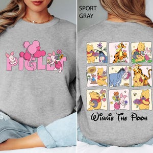 May include: Sport grey sweatshirt with the word "Piglet" in pink, a cartoon pig, and balloons. The back displays a grid of Winnie the Pooh characters, including Pooh, Tigger, and Eeyore, with the words "Winnie The Pooh" underneath.