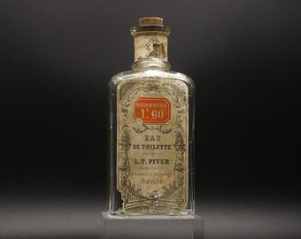 May include: An antique Eau de Toilette bottle with a cork stopper. The clear glass bottle features a faded label with French text and a red and white emblem. The label reads "MAISON UNIVERSELLE 1.60" and "L.T. PIVER PARFUMEUR PARIS."