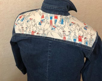 May include: A dark blue denim jacket with a white shoulder panel featuring a horse racing scene in red, blue, and black. The jacket has a classic collar and long sleeves. The back of the jacket is visible.