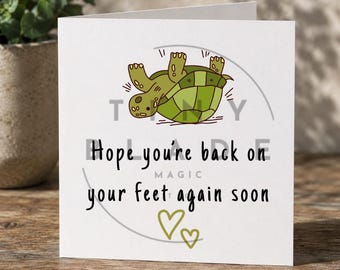 Può includere: Biglietto di auguri bianco con una tartaruga dei cartoni animati verde sulla schiena. Il testo recita: "Spero che tu ti rimetta presto in piedi" con due cuori verdi. Il testo è nero.
