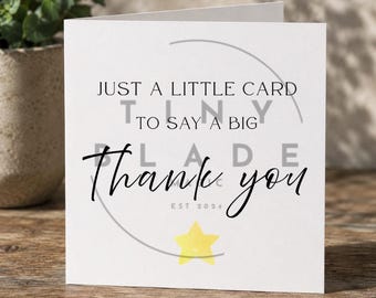 Può includere: Un biglietto di auguri bianco con la scritta "JUST A LITTLE CARD TO SAY A BIG Thank you" in corsivo nero. In basso c'è una stella gialla. Il biglietto è su una superficie di legno.
