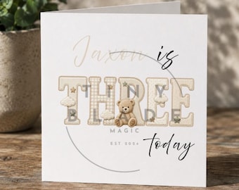 Può includere: Biglietto di compleanno bianco con la scritta "Jaxon compie TRE oggi". La parola "THREE" è in un design patchwork con un orsacchiotto. La carta include anche le parole "MAGIC" e "EST 2024".