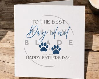 Può includere: Biglietto di auguri bianco con la scritta "TO THE BEST Dog Dad" in blu. Presenta due impronte di zampe blu e le parole "HAPPY FATHERS DAY". Il biglietto è su una superficie di legno.