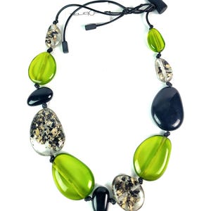 May include: A necklace featuring a series of smooth, pebble-shaped beads in translucent lime green, solid black, and clear resin with embedded black and gold-toned flecks. The beads are strung on a thin black cord with a toggle closure.