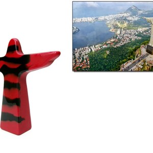 May include: A red and black abstract sculpture of a figure with outstretched arms, resembling the Christ the Redeemer statue. The background shows an aerial view of Rio de Janeiro, Brazil, with the Christ the Redeemer statue on a hilltop.