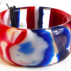 Może przedstawiać: Pierścień w paski w kolorze czerwonym, białym i niebieskim wykonany z przezroczystego plastiku. Paski są zmieszane, tworząc efekt marmuru.