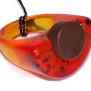 May include: A pendant necklace featuring a unique, abstract design. The pendant is a vibrant combination of orange and red hues, with a dark brown circular accent. The necklace is suspended from a black cord.