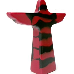 May include: A decorative, abstract sculpture in a cross-like shape. The sculpture features a vibrant red and black marbled pattern. The design includes a tall, rectangular base and a wider top with extended arms, creating a unique artistic piece.