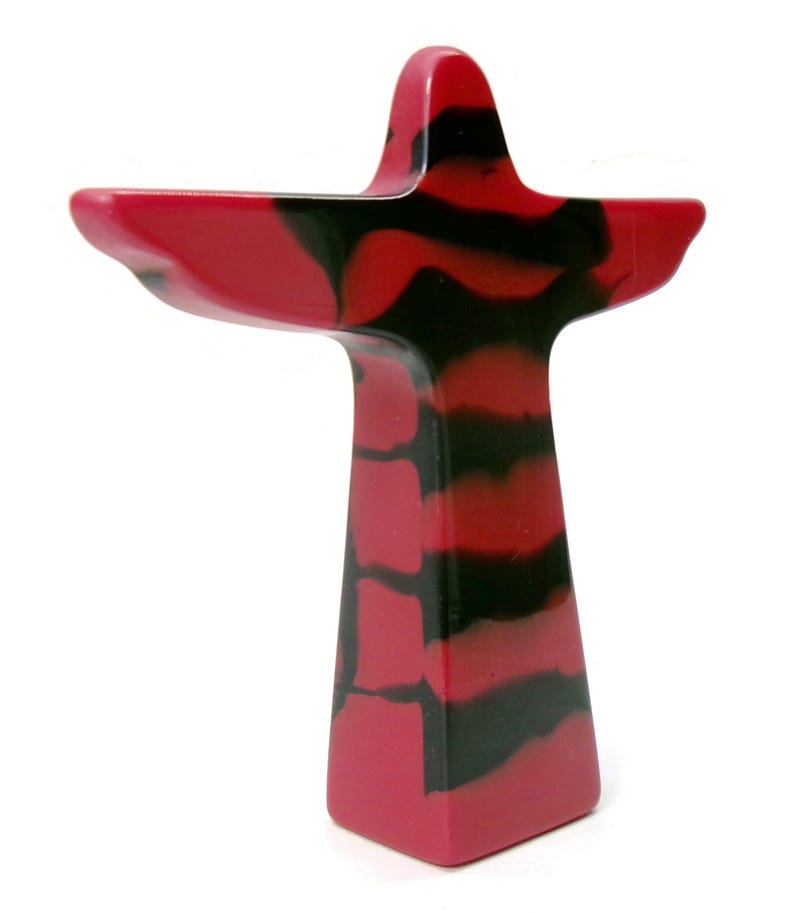 May include: A decorative, abstract sculpture in a cross-like shape. The sculpture features a vibrant red and black marbled pattern. The design includes a tall, rectangular base and a wider top with extended arms, creating a unique artistic piece.
