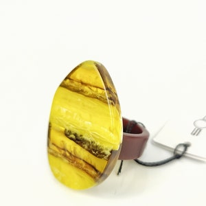 May include: A large, teardrop-shaped ring with a yellow and brown stone. The stone has a layered appearance with varying shades of yellow and brown. The ring's band is a dark reddish-brown color.