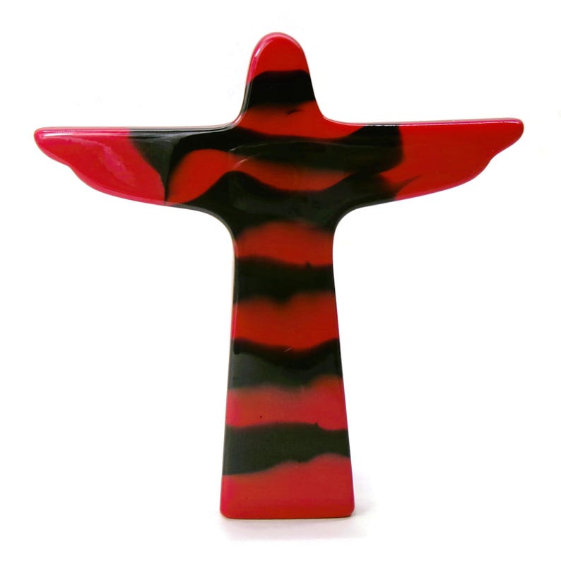 May include: A red and black decorative figurine in the shape of a person with outstretched arms. The figurine has a glossy finish and a striped pattern of red and black. The design is reminiscent of the Christ the Redeemer statue.